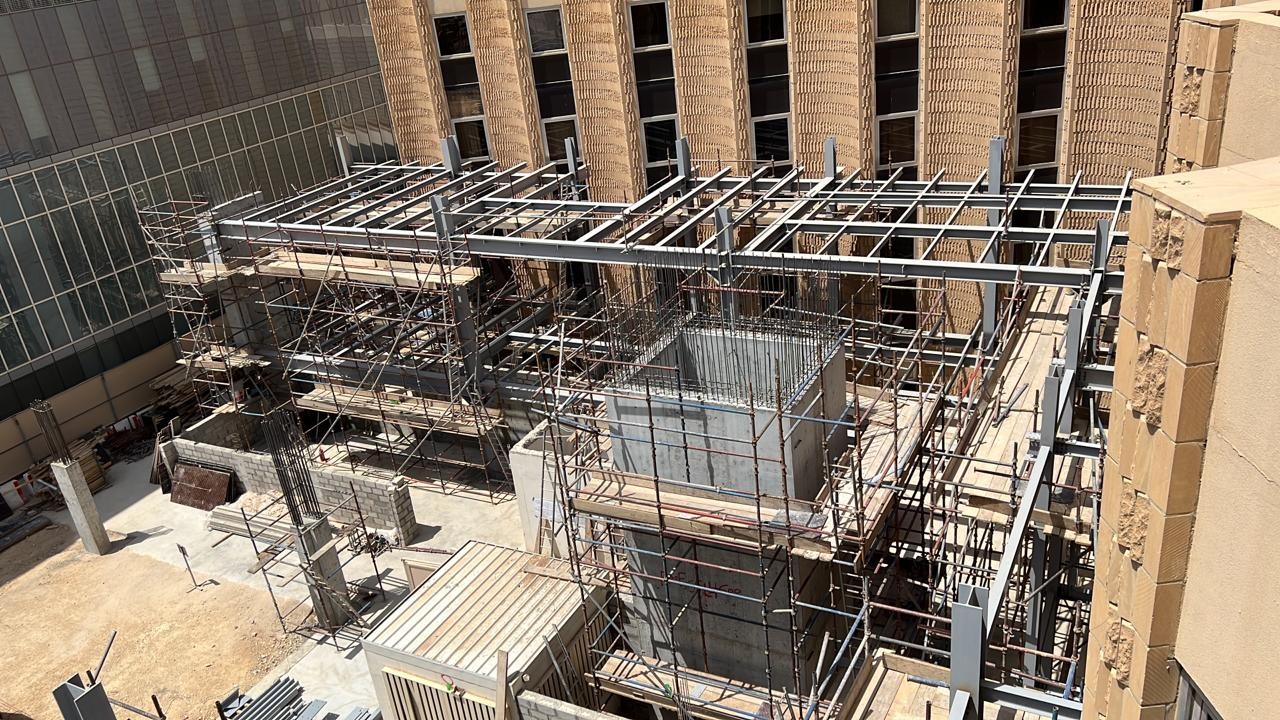 Steel structure mid-construction showing scaffolding and hospital buildings